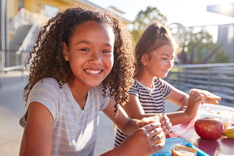 Girlfriends at school lunch table, one smiling to camera